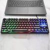 Black mechanical keyboard with rainbow backlighting connected to a laptop on a desk
