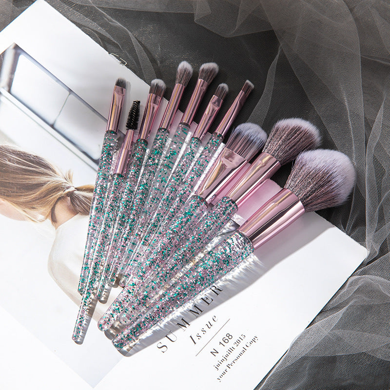 Blue glitter-handled makeup brushes fanned over a magazine and grey mesh fabric