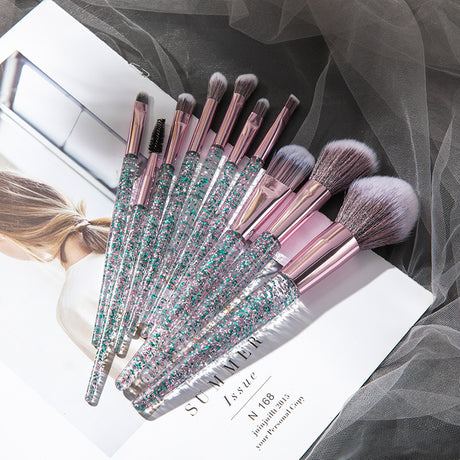 Blue glitter-handled makeup brushes fanned over a magazine and grey mesh fabric