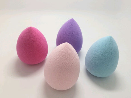 Four teardrop sponges in pink, pale pink, purple and blue on a white surface