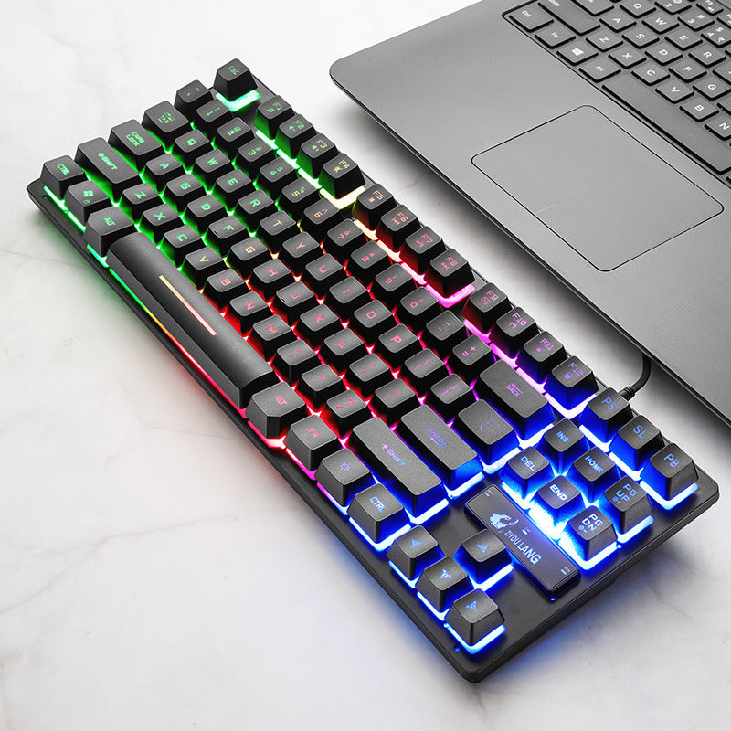 Angled black mechanical keyboard with rainbow backlighting beside a laptop