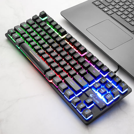 Angled black mechanical keyboard with rainbow backlighting beside a laptop