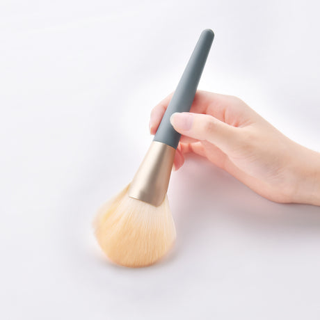 Hand holding a large makeup brush with blue handle and pale bristles