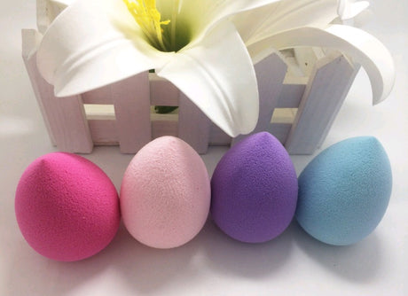 Four coloured teardrop sponges in front of a white flower and basket