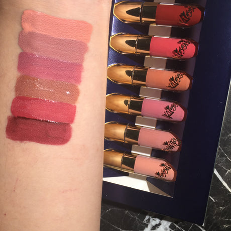 Six lipsticks beside matching colour swatches on an arm