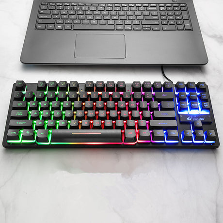 Black mechanical keyboard with rainbow backlighting connected to a laptop on a desk