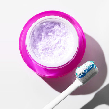 Top view of open pink powder jar with loaded toothbrush