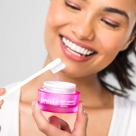 Woman holding open pink Smilekit tooth powder jar and toothbrush