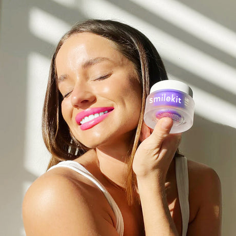 Woman holding a closed Smilekit powder jar beside her face