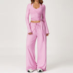 Women's pink long sleeve wrap top worn with matching wide leg trousers.