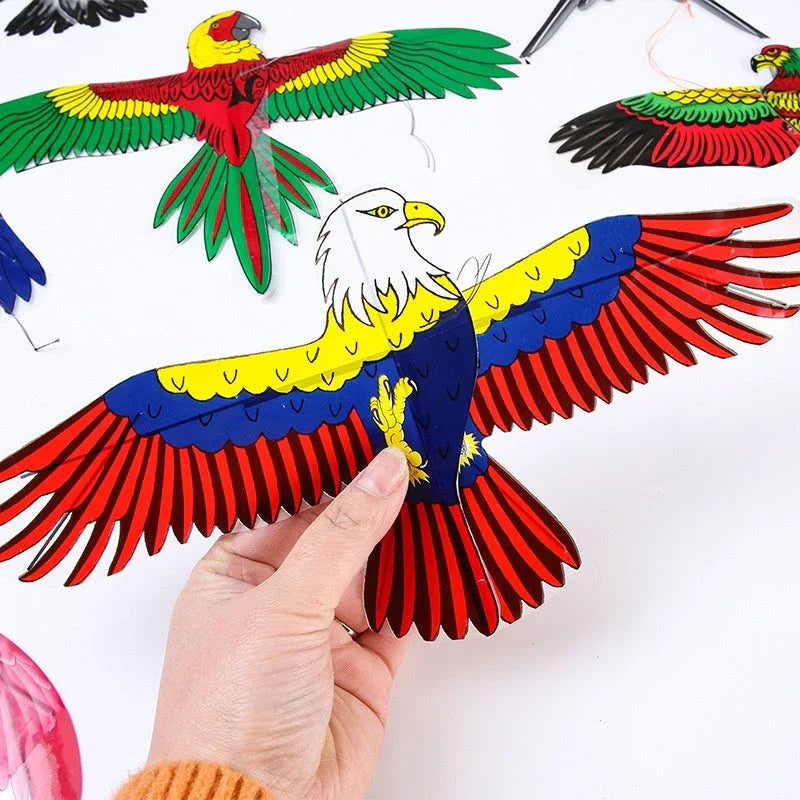 Hand holding a red, yellow and blue eagle kite among other bird kites